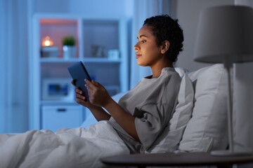 technology, internet and people concept - young african american woman with tablet pc computer lying in bed at home at night