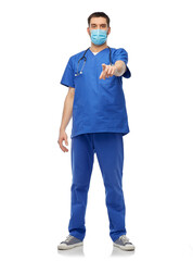 healthcare, profession and medicine concept - doctor or male nurse in blue uniform, face protective medical mask for protection from virus disease and gloves pointing to camera over white background