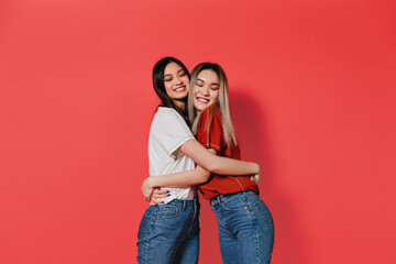 Charming long-haired girls are smiling and hugging against red background