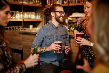 Group of cheerful friends standing near bar counter, drinking beer and chatting.