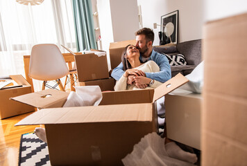 Smiling young couple move into a new home sitting on floor and unpacking boxes of their belongings.
