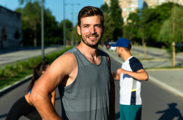 Fototapeta na wymiar Portrait of man in sports clothing standing and looking at camera after morning workout in the city with his friends in background.