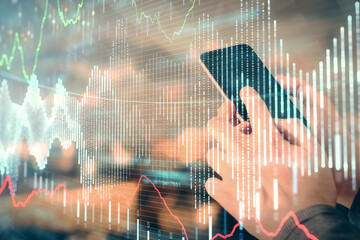 Double exposure of man's hands holding and using a digital device and forex graph drawing. Financial market concept.