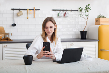 attractive young woman working with laptop in the kitchen, drinking coffee