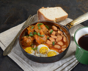Meatballs in a frying pan, scrambled eggs and beans in a tomato on a dark background. Rustic style.

