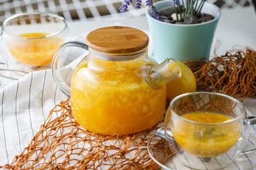 rich teapot of citrus tea with orange and lemon on a light background with two cups of tea