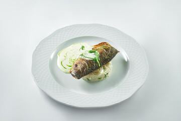 Appetizing mackerel fillet with creamy rice and white sauce in a white plate on a white plate