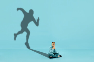 Childhood and dream about big and famous future. Conceptual image with boy and shadow of sportive male runner, champion on blue background. Childhood, dreams, imagination, education concept.
