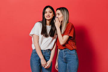 Asian women in loose T-shirts gossip on red background
