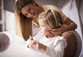 Mother and daughter in bedroom. Little girl drawing.