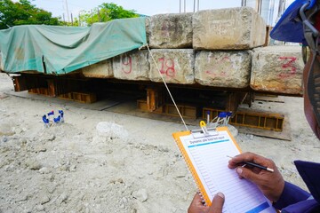 Engineers are recording the subsidence of pile foundation on the form as part of the Dynamic load test by using large cement blocks to press down on the pile.