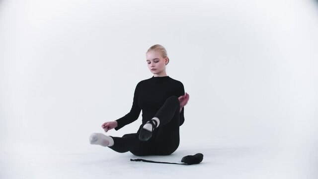 Young blonde woman ballerina takes off her pointe shoes