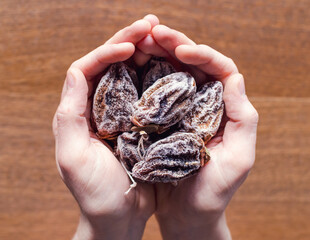 A bunch dried persimmons fruits in the hands on the wooden  background. Horizontal frame, selective focus.