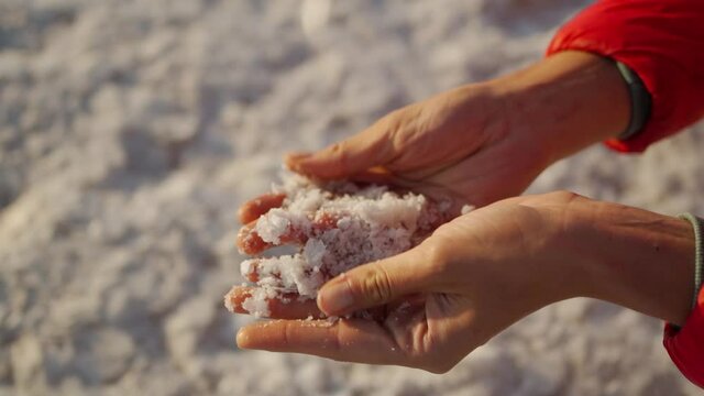 Top view slow motion closeup woman hands holding crystallized salt natural mineral formation at Dead Sea coastline with highlight sunlight