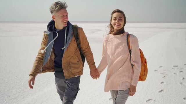 happy lovely couple travelers walking hand to hand on dazzling pink white salty coast of Sivash Pink Salt Lake. traveling to Lemurian Pink mineral salt lake, Southern Ukraine