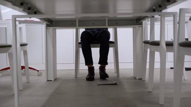 Legs of unrecognizable nervous man moving under office table indoors. Anxious young businessman employee sitting in conference room. Worries and business stress concept.