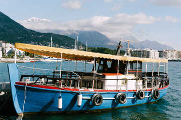 Wooden tourist boat moored against the backdrop of Porto Montenegro and the snow-capped peak of Mount Lovcen.