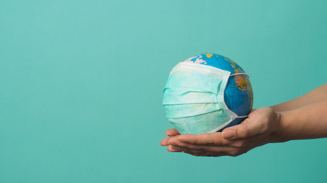 Hand is holding earth globe and face mask on green or Tiffany Blue background.covid-19 concept.