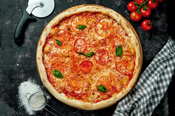 Appetizing Italian pizza with cheese, tomatoes, basil and red sauce in a composition with ingredients on a black background. Pizza margarita