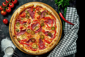 Appetizing italian pizza with ham, cheese, jalapenos, tomatoes and bell pepper in a composition with ingredients on a black background
