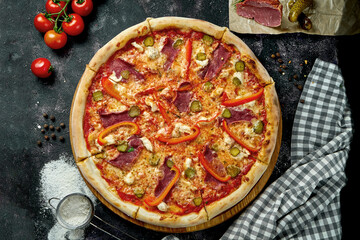 Appetizing italian pizza with cheese, bell pepper, ham, pickled cucumbers and red sauce in a composition with ingredients on a black background