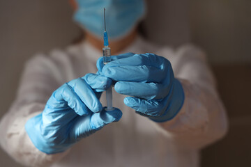Nurse in medical gloves and a mask prepares a syringe for injection against omicron strain....