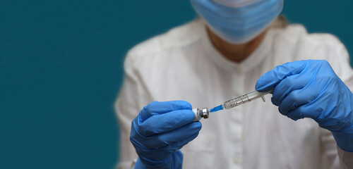 Nurse wearing in medical gloves and facemask fills a syringe from vial of  vaccine against omicron...