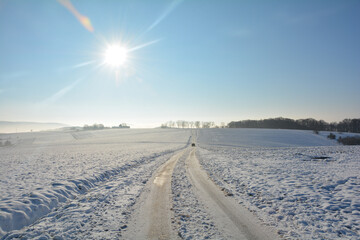 Snow-covered road in the country, with a moving car, a lot of snow in the fields