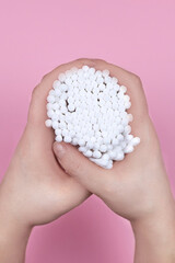 White cotton ear buds in the hands of a woman on a pink background.