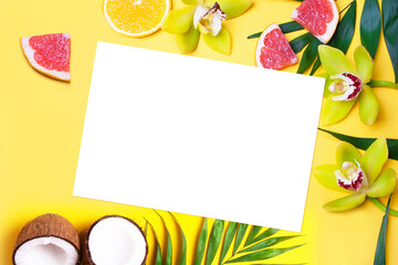 Blank white leaf on a background of yellow orchids, palm leaves, grapefruit and coconuts on a yellow background. Mock up. Flat lay style