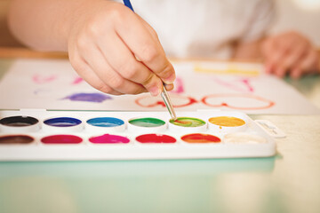 Fototapeta na wymiar children's hand art brush in paint with palette of watercolors slective focus, film noise