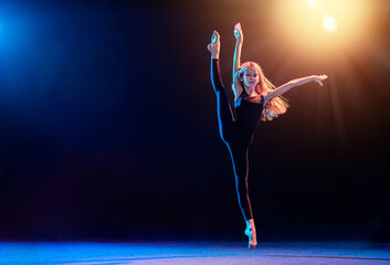 ballet girl in tight-fitting suit jumping on black background with her long hair loose, the...