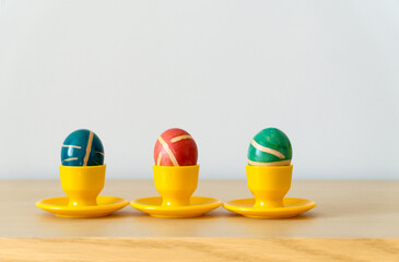 Three colorful painted homemade easter eggs with modern pattern on yellow coasters on wooden table. Easter decoration, easter background  with copy space.