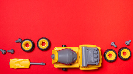 A set of parts and tools to collect the designer of the truck mixer machine on a red with copyspace for text. The screwdriver and cogs of the machine, which can be disassembled and assembled