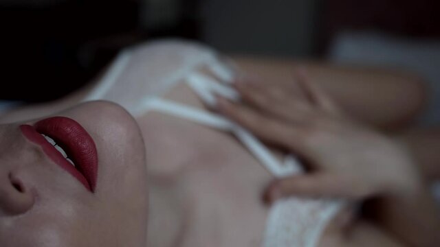 excited sexy woman is caressing herself in bedroom, closeup view on open lips and body