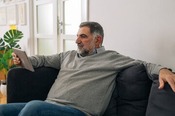 Fototapeta premium man sitting on sofa in his home and using digital tablet