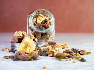 Glass jar of nuts, trail mix, granola, banana chips, dried fruit, chocolate chips, almonds, peanuts, walnuts and sunflower seeds.  Healthy good carbs and fat, snack food.