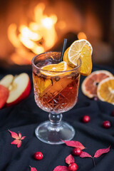 Hot autumn cocktail with orange and apple, mulled wine with cinnamon sticks and anise with fireplace in the background