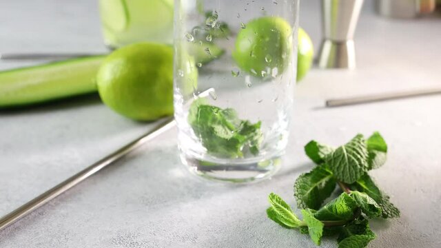 Preparing mojito cocktail or detox cocktail of mint, cucumber and lime in highball glass on a gray concrete stone surface background. Camera moving along glass.