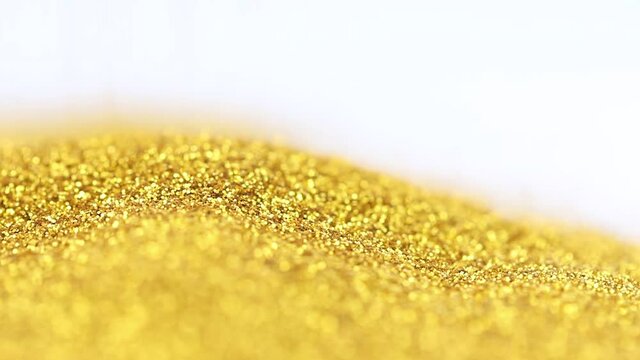 Scattering of shimmery fine round gold glitter on a white surface in close-up. Pouring a strip of sparkling sparkling gold glitter onto the surface with copy space.