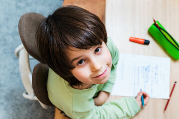 Young school boy doing his homework sitting at the table at home. Concentrated child writing exercises with pleasure. Homeschooliong concept.