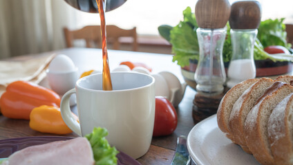 Coffee is poured into a cup. Sandwich with ham and green salad on a plate. Kitchen table. Breakfast. Close-up. Soft focus in the background
