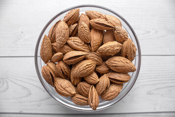 A pile of almonds in a plate close-up. Salted fresh nuts in the shell in a glass container. Top view. The texture of the almonds.