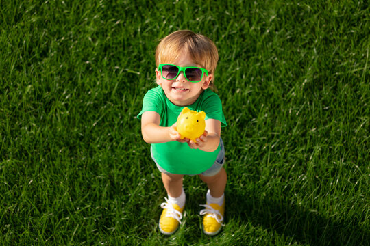 Child holding piggy bank in hands against green spring background