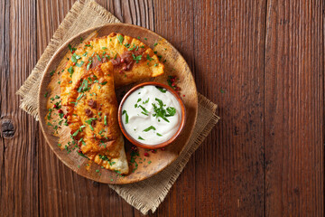 Traditional cheebureki, served on a wooden plate with sauce.