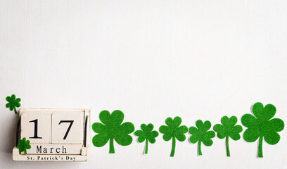 Happy St. Patrick's Day concept, wooden calendar with green paper clover leaf on white wooden background. Flat lay, top view with copy space.
