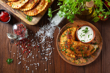 Traditional cheebureki, served on a wooden plate with sauce.