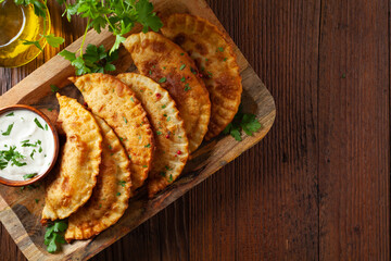 Traditional cheebureki, served on a wooden plate with sauce.
