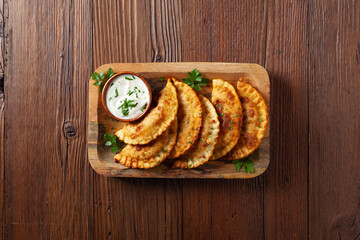 Traditional cheebureki, served on a wooden plate with sauce.