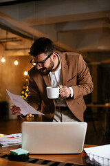 Young businessman using laptop and drinking coffee in his office. Handsome man on coffee break